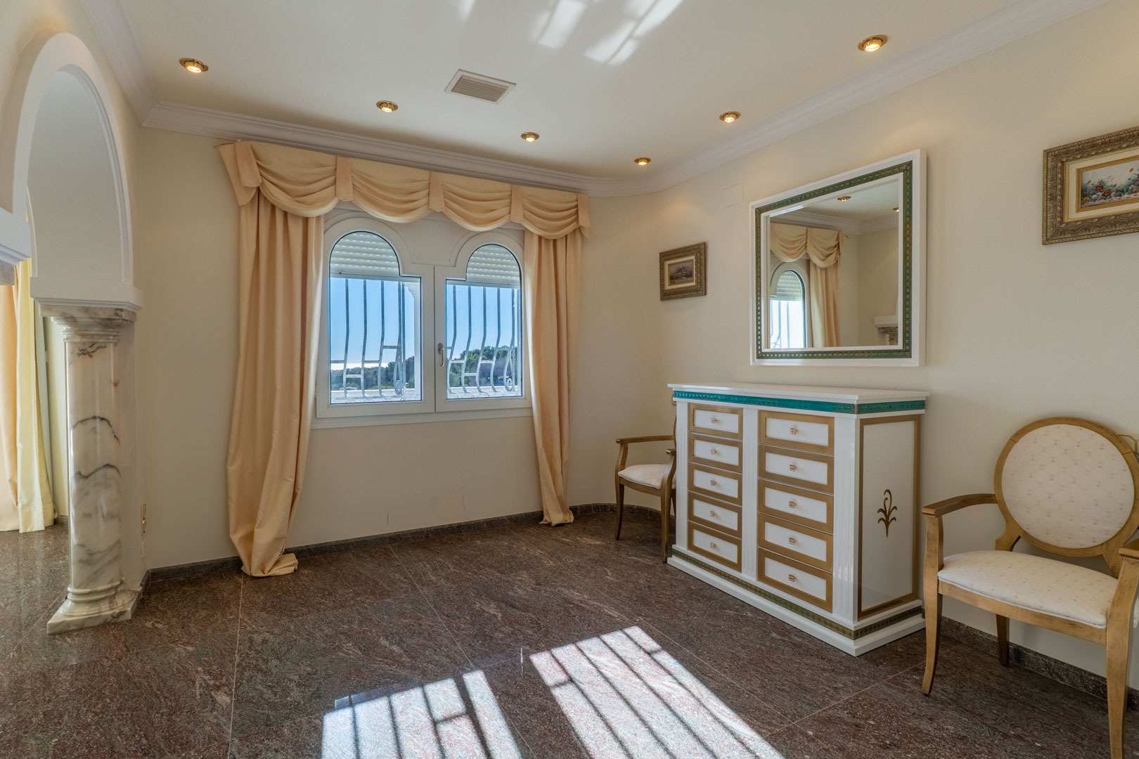 Elegante kamer met gepolijste granieten vloer, een klassieke ladekast en een marmeren zuil naast een boogvenster met veel natuurlijk licht.