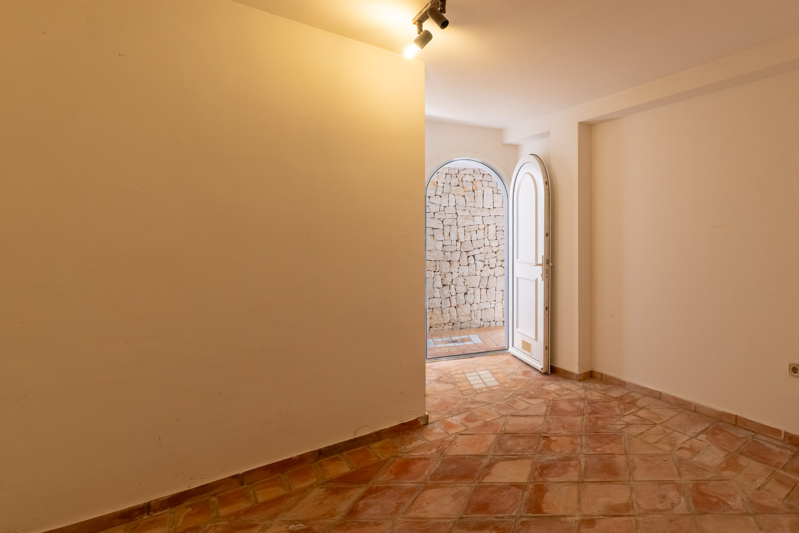 Functionele ruimte met traditionele terracotta vloertegels en een boogdeur die uitkomt op een binnenplaats met een natuurstenen muur.