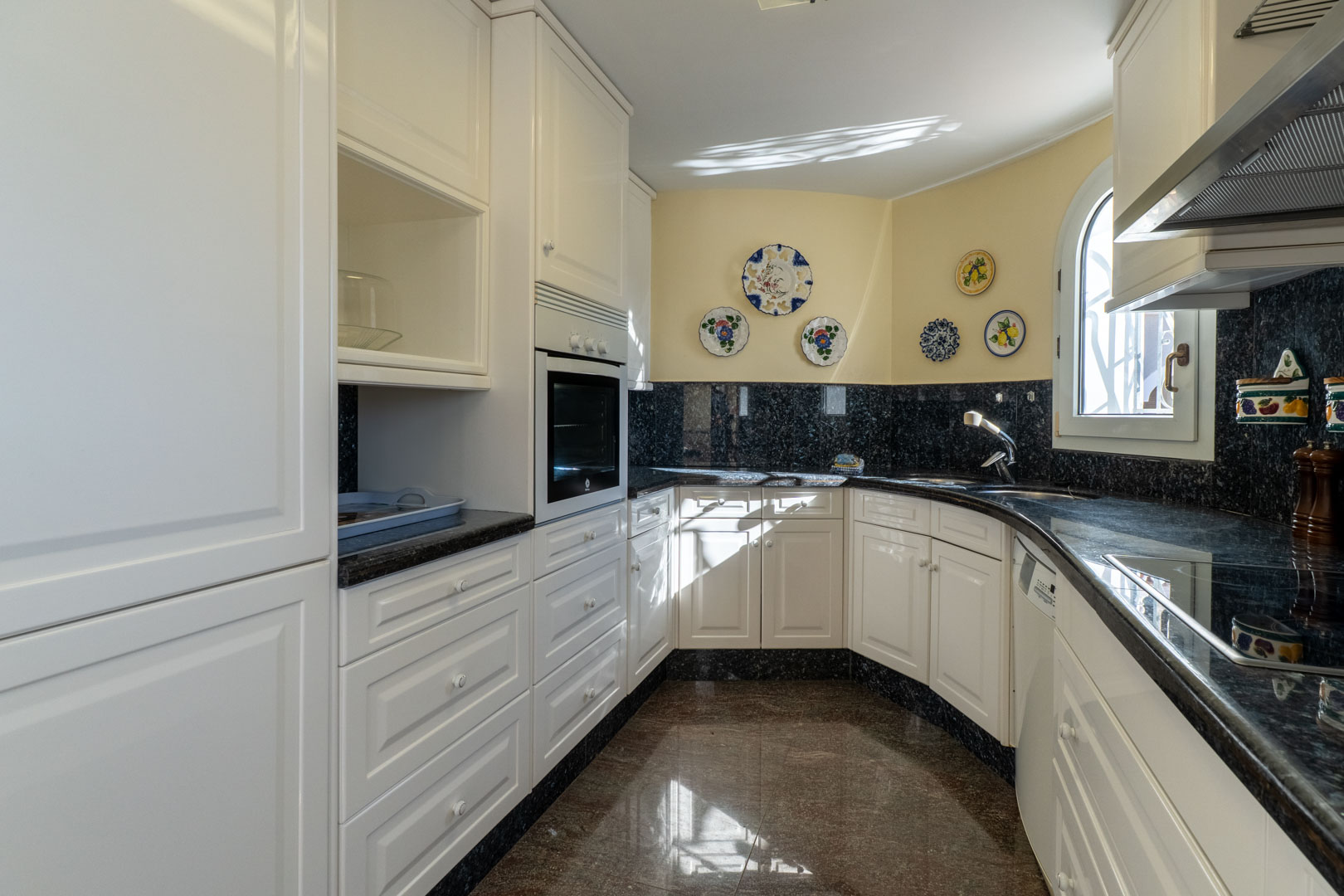 Onafhankelijke keuken met witte kasten, een donker granieten werkblad en decoratieve borden. Voorzien van een rond raam en geïntegreerde inbouwapparatuur.