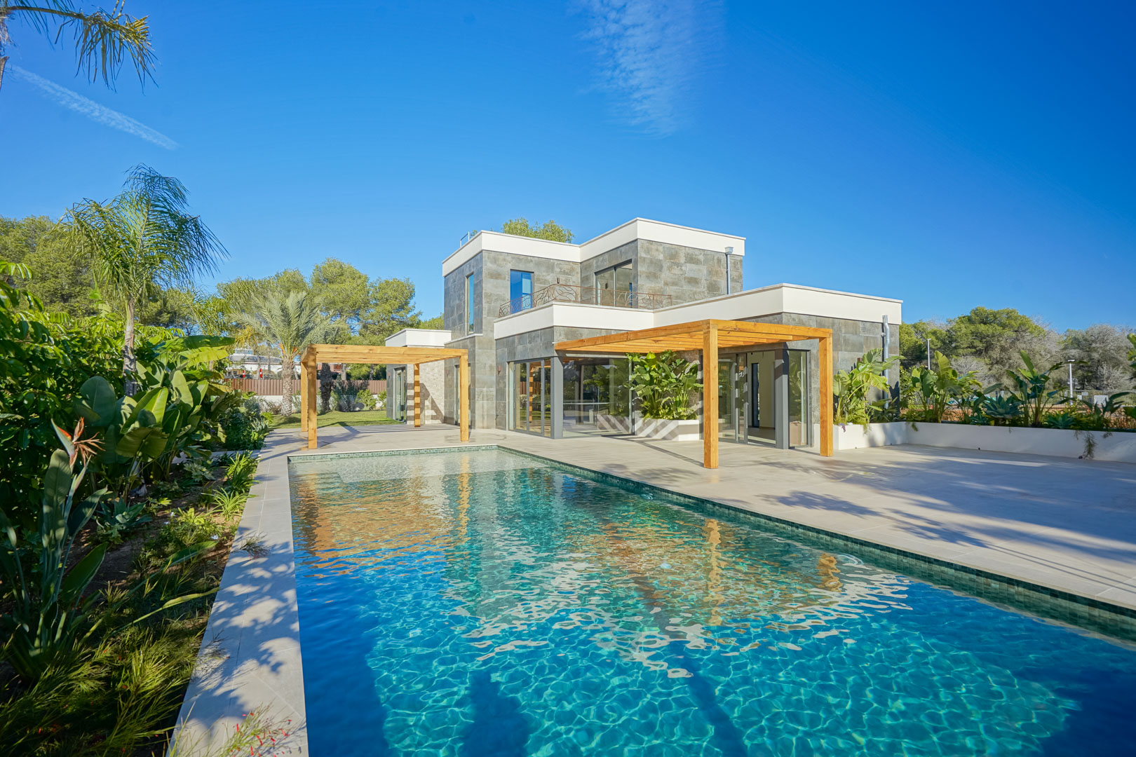 Exterieur van de villa met zwembad in Bali-stijl, ruime terrassen en iroko houten pergola's te midden van een mediterrane tuin.