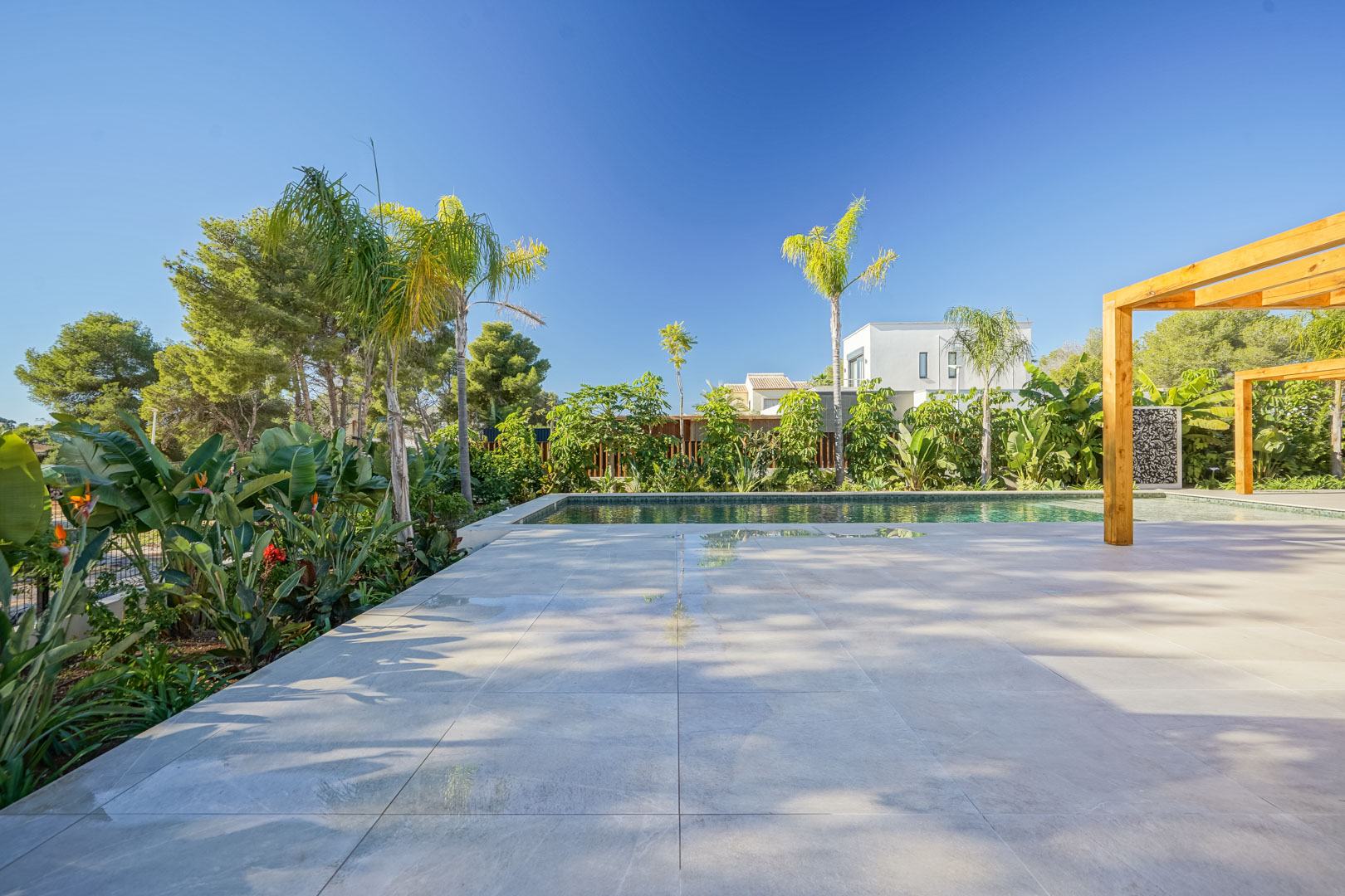 Groot terras met keramische tegels naast een zwembad in Bali-stijl, voorzien van iroko houten pergola's en een weelderige mediterrane tuin.