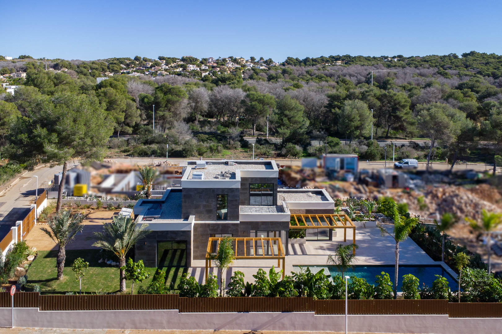 Luchtfoto van de moderne villa met stenen gevel, iroko houten pergola's, zwembad in Bali-stijl en mediterrane tuin in een groene omgeving.