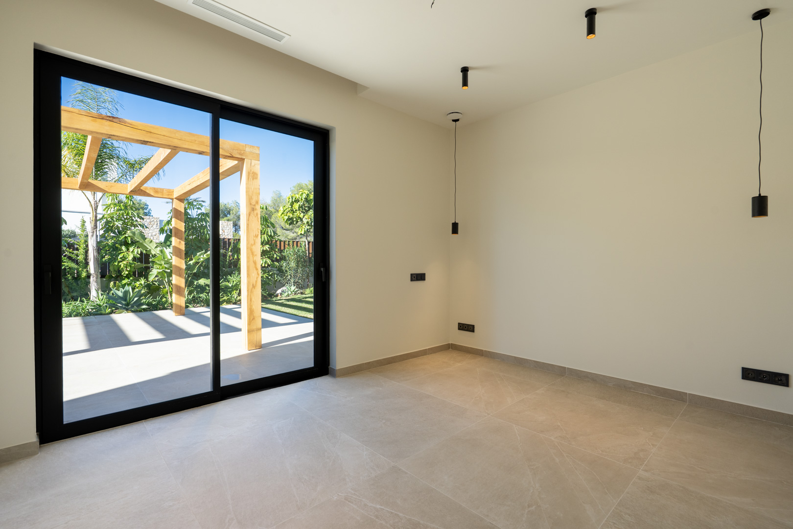 Minimalistisch interieur met keramische vloer en grote schuifpui naar het buitenterras met houten pergola en mediterrane beplanting.