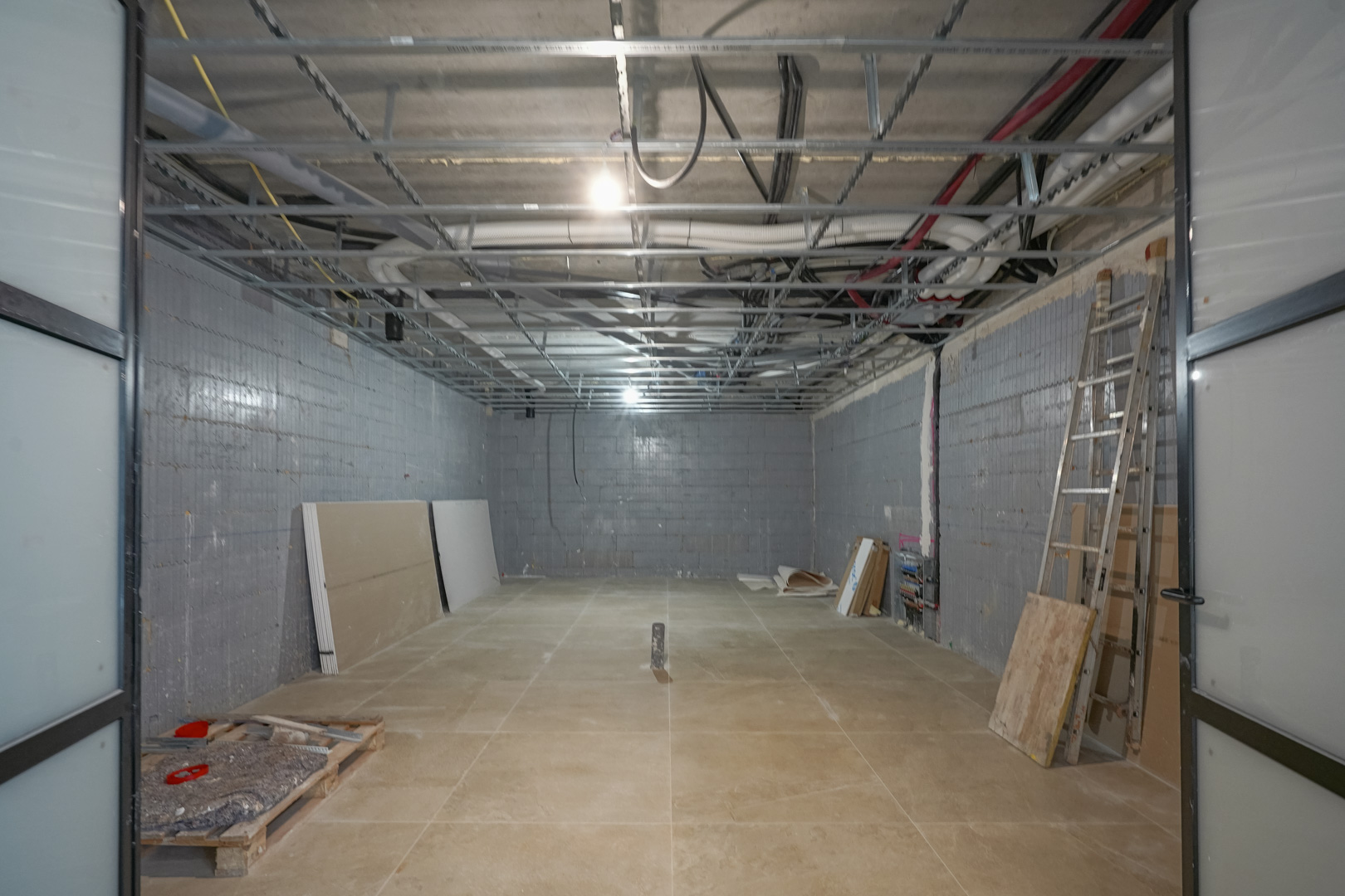 Ruime kelder van 180 m2 in aanbouw met isolerende Styro Stone wanden, zichtbare technische installaties en grote schuifdeuren met zwart profiel.
