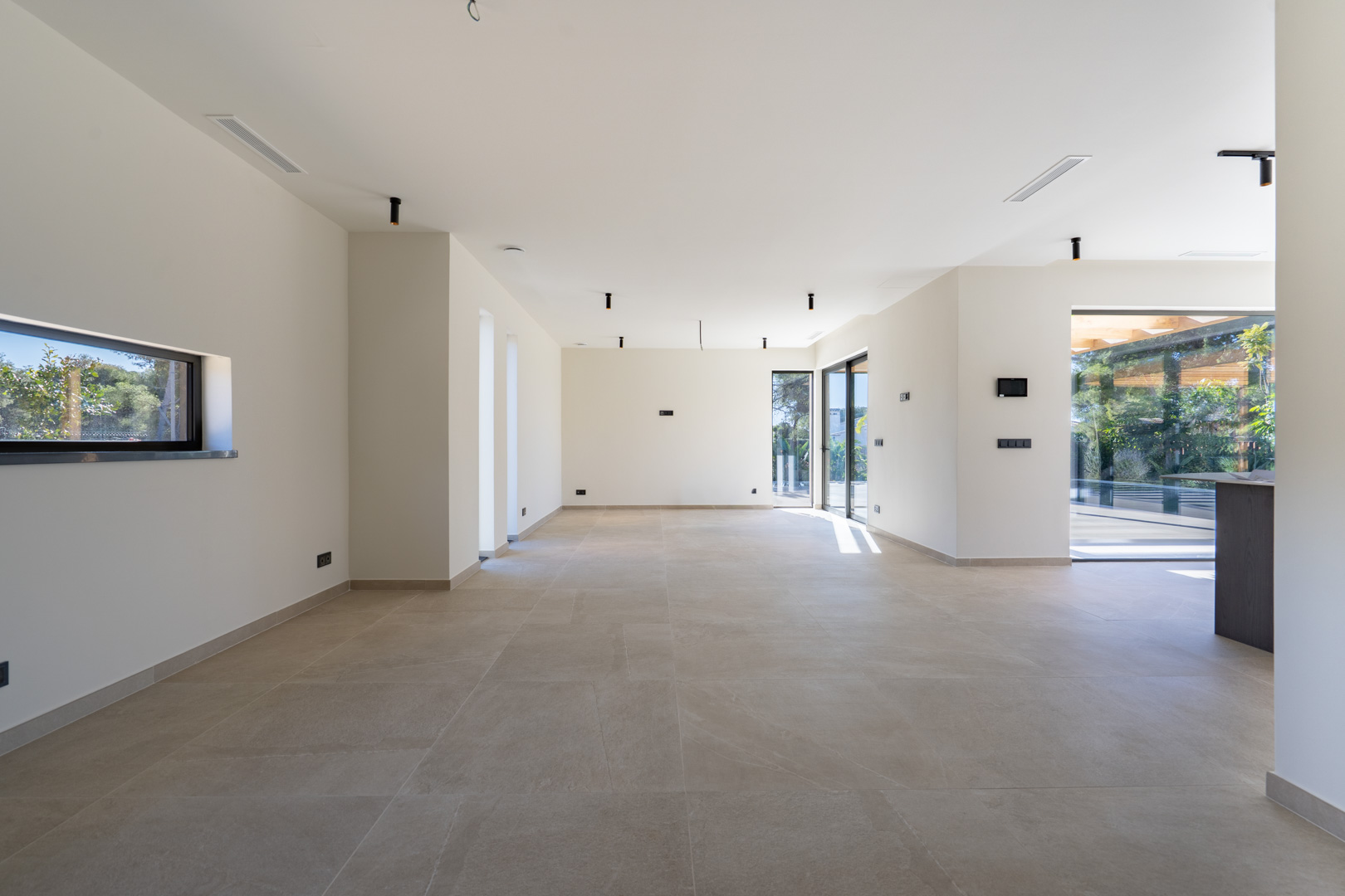 Ruime open woonkamer met grootformaat vloertegels, minimalistische verlichting en grote schuifpuien die direct toegang bieden tot het terras.