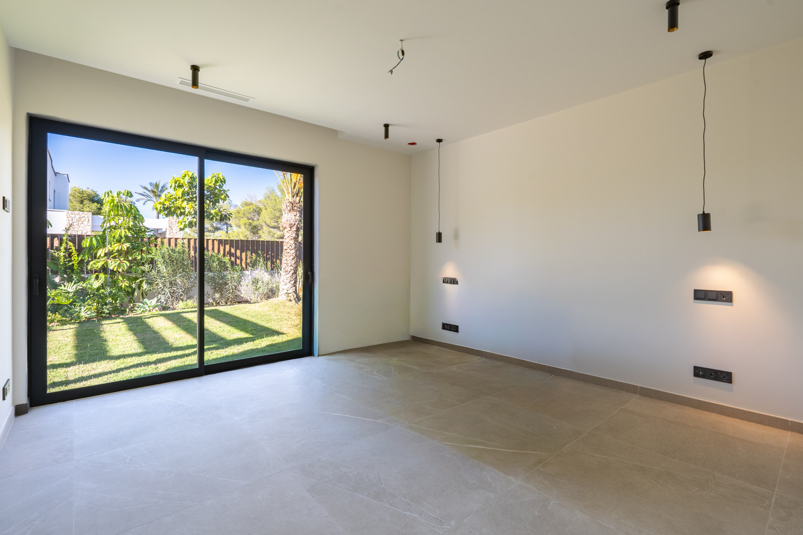 Slaapkamer met porseleinen tegelvloer en grote schuifpui naar de tuin. Voorzien van minimalistische zwarte hanglampen en geïntegreerde airconditioning in het plafond.