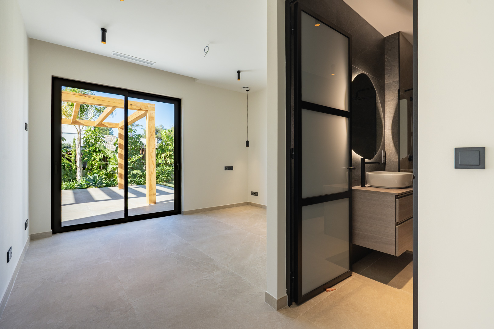 Slaapkamer met toegang tot het terras en houten pergola. Voorzien van en-suite badkamer met opzetwastafel, verlichte spiegel en zwarte aluminium profielen.