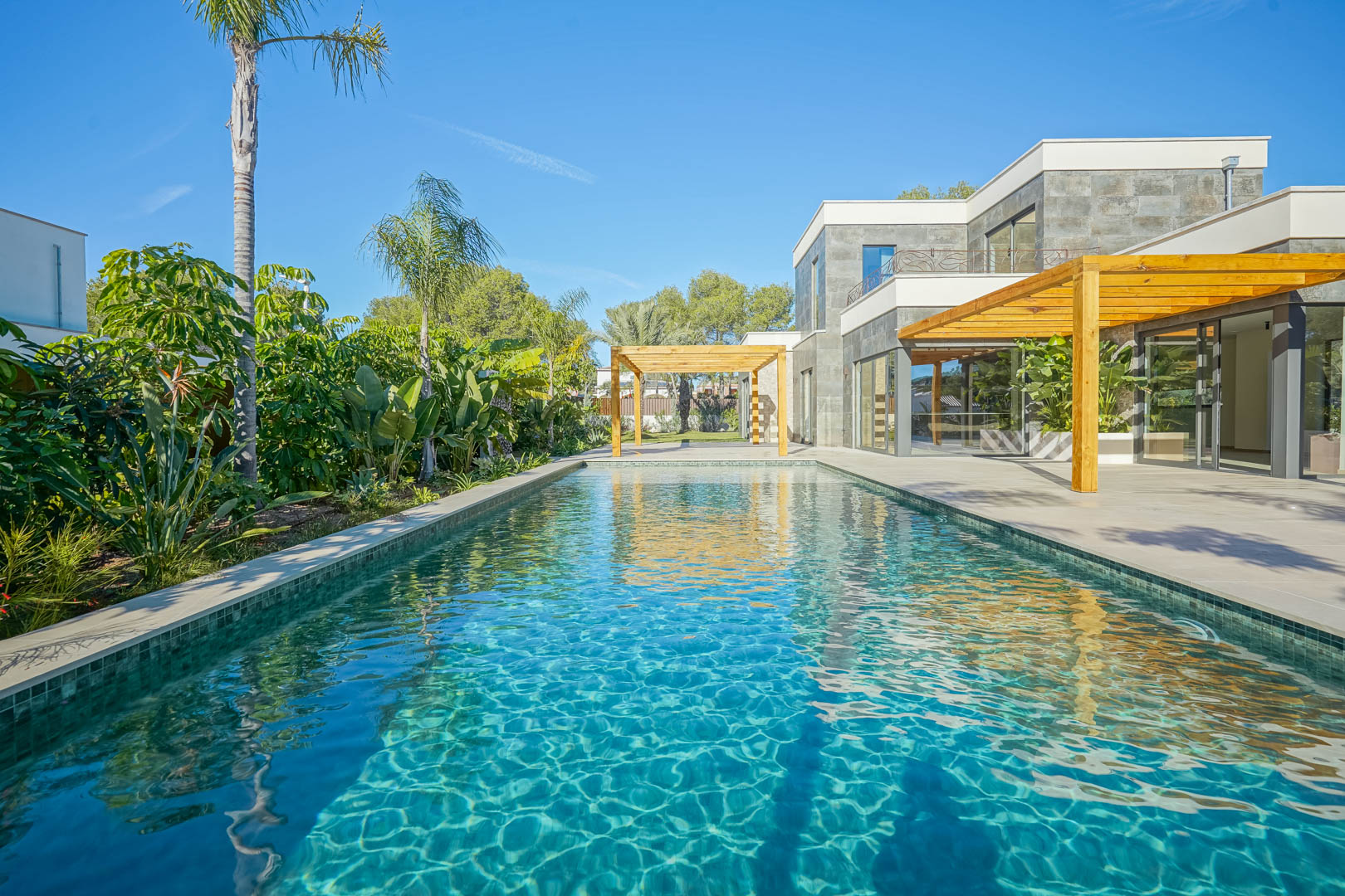 Zwembad in Bali-stijl met smaragdgroene tegels, voorzien van een ruim terras met iroko houten pergola's en een weelderige mediterrane tuin.