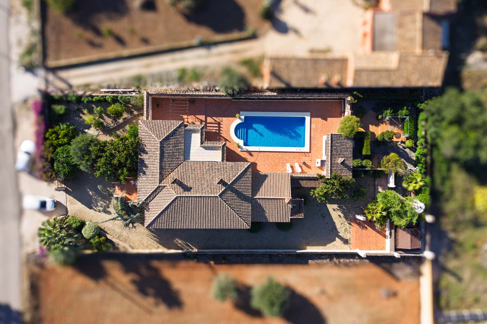 Bovenaanzicht van de villa op een vlak perceel, met een rechthoekig zwembad, ruime geplaveide terrassen en een traditioneel pannendak.