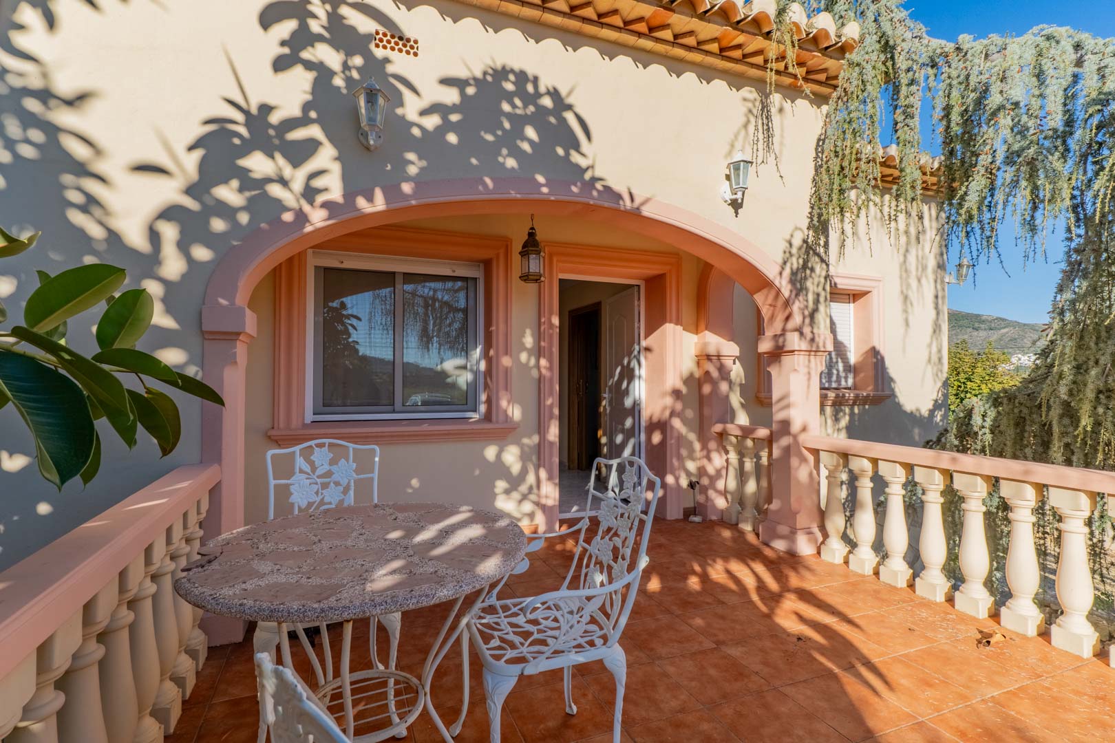 Buitenterras met mediterrane bogen, terracotta vloeren en wit smeedijzeren meubilair, gekenmerkt door een natuurlijk spel van licht en schaduw.
