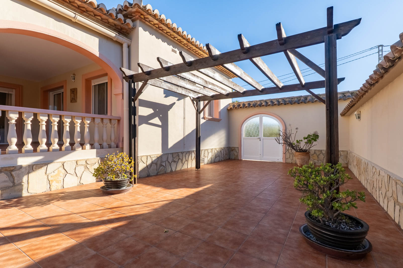 Buitenterras met terracotta tegels, een houten pergola en muren met natuurstenen plint. Het biedt toegang tot de verhoogde naya met balustrade.
