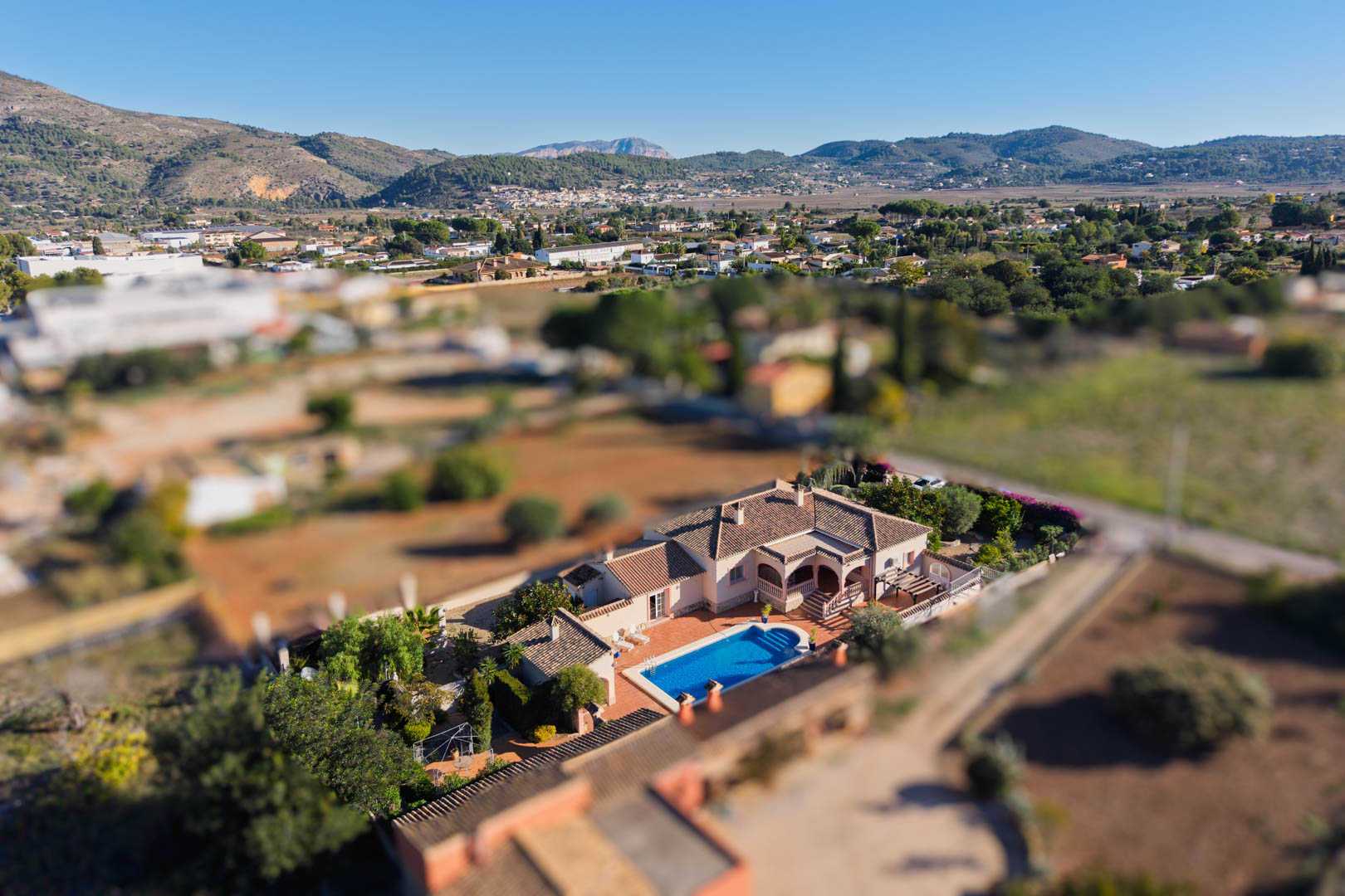 Luchtfoto van de mediterrane villa in Jalón, met het privézwembad, het terras en het vlakke perceel gelegen in het bergachtige landschap van de vallei.