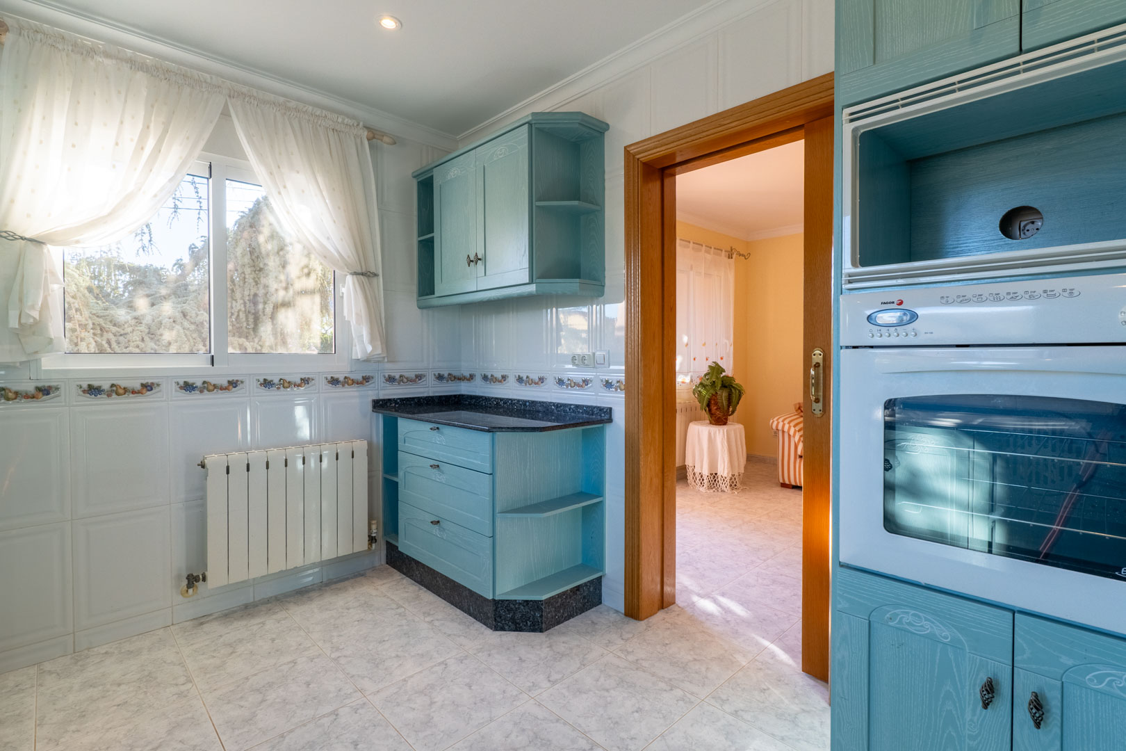 Onafhankelijke keuken met lichtblauwe kasten, een donker granieten werkblad, wit betegelde wanden en een houten doorgang naar de woonkamer.