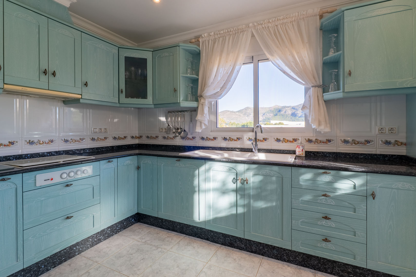 Onafhankelijke keuken met turquoise kasten, een donker granieten werkblad en een raam met vrij uitzicht op de bergen van de Jalón-vallei.