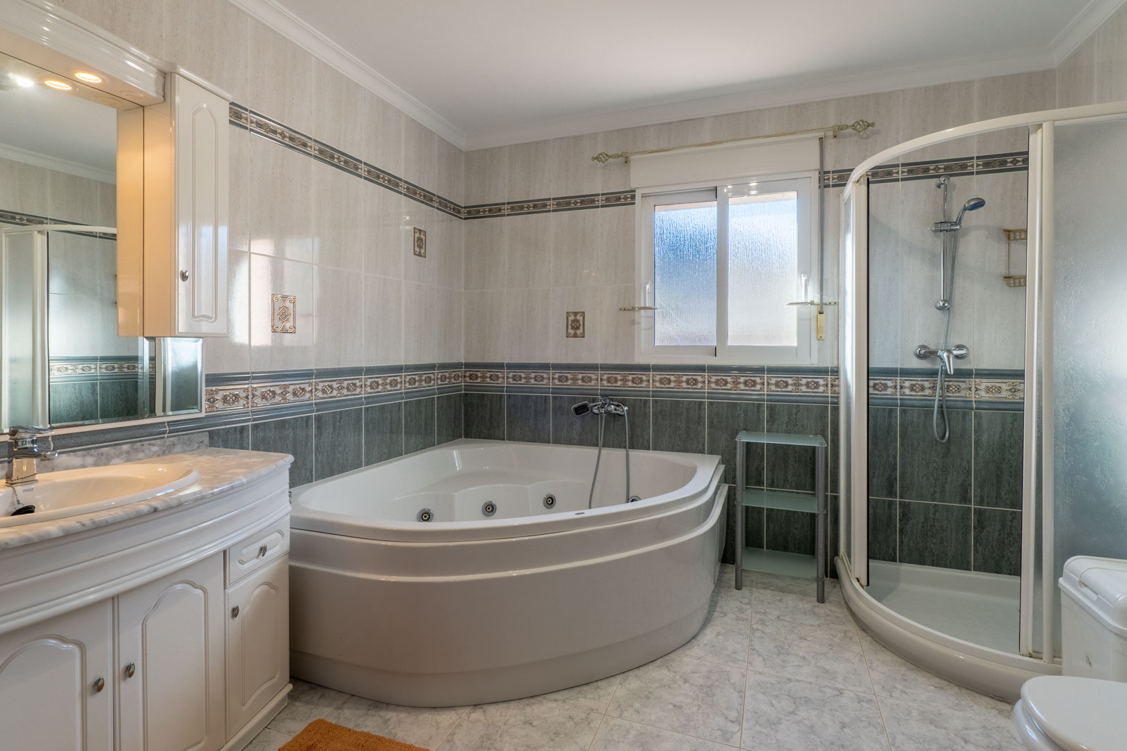 Volledige badkamer met een hoek-whirlpoolbad, aparte halfronde douchecabine en een wastafelmeubel met marmeren blad en tweekleurige betegeling.