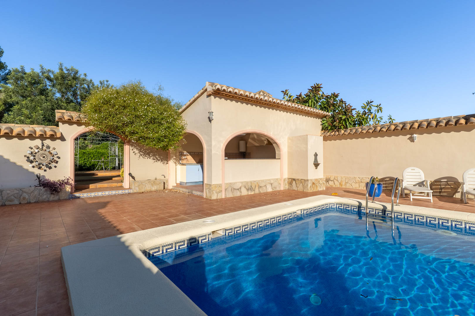 Zwembadgedeelte met terracotta terras, een overdekte buitenkeuken met bogen en natuurstenen details in een mediterrane setting.