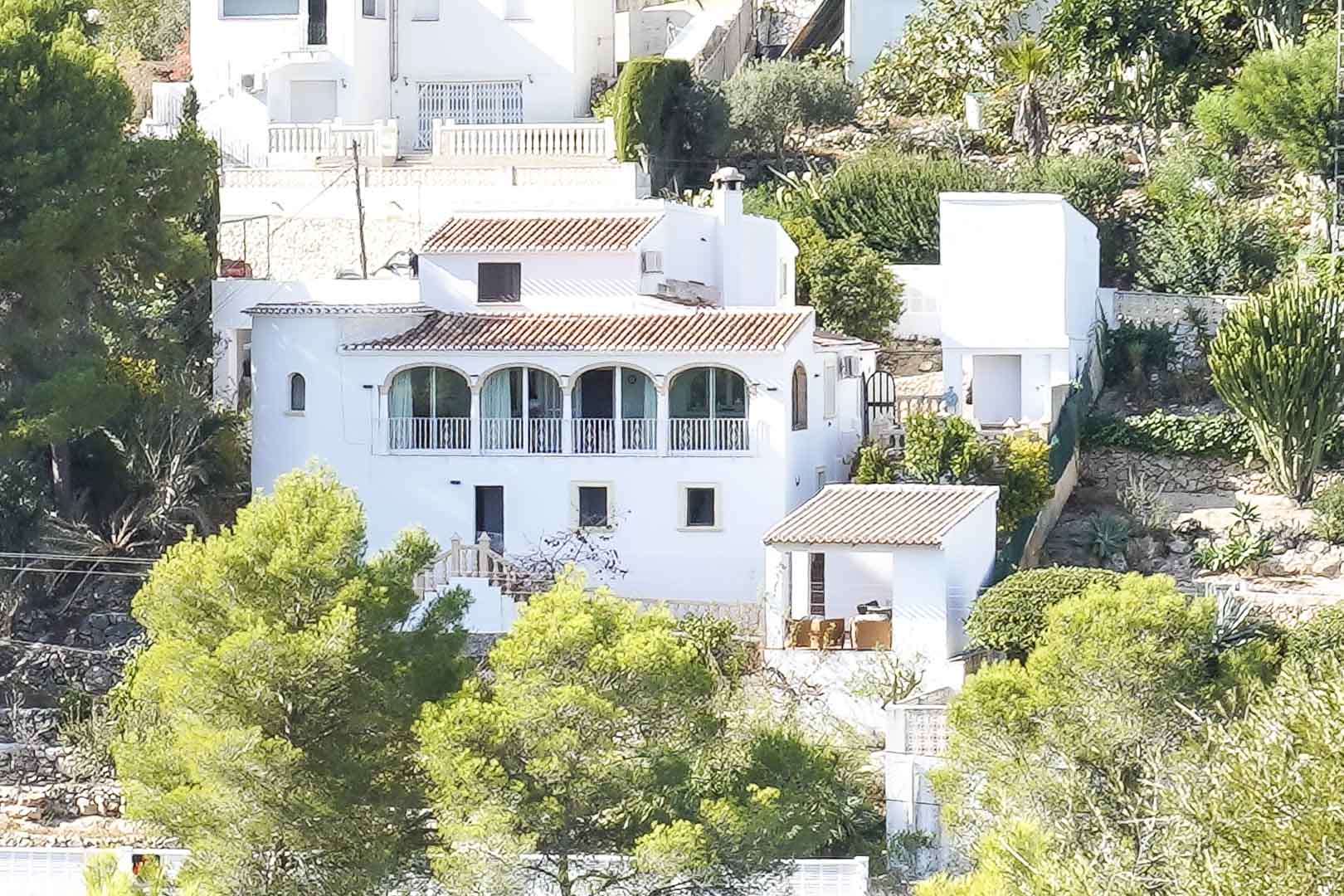 Exterieur van de witte villa met traditionele pannendaken en een naya met bogen, gelegen op een helling te midden van mediterrane pijnbomen.