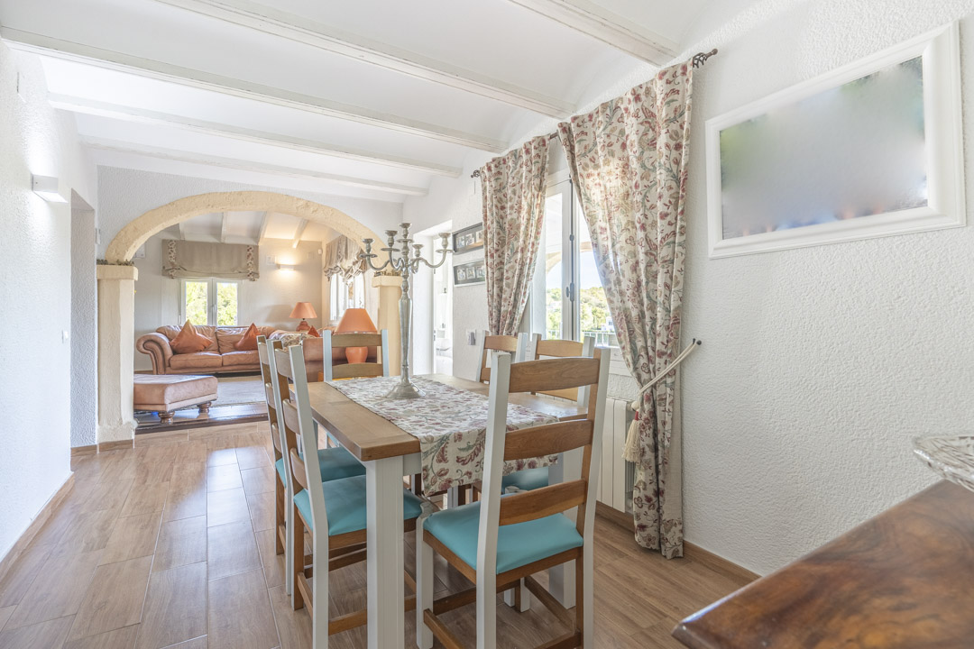 Lichte eetkamer met witte balkenplafonds en een Tosca-stenen boog naar de woonkamer. Voorzien van houtlook vloertegels en rustiek meubilair.