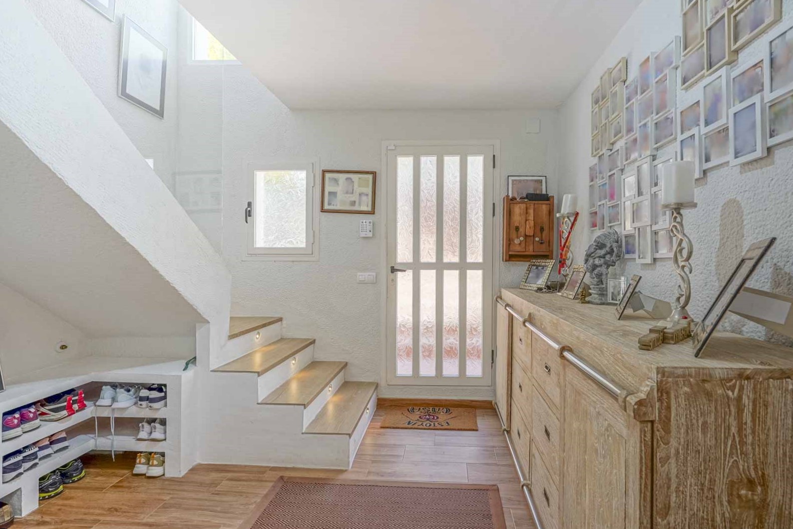 Lichte hal met houten trap voorzien van geïntegreerde LED-verlichting, een rustiek houten dressoir en praktische schoenenopslag onder de trap.