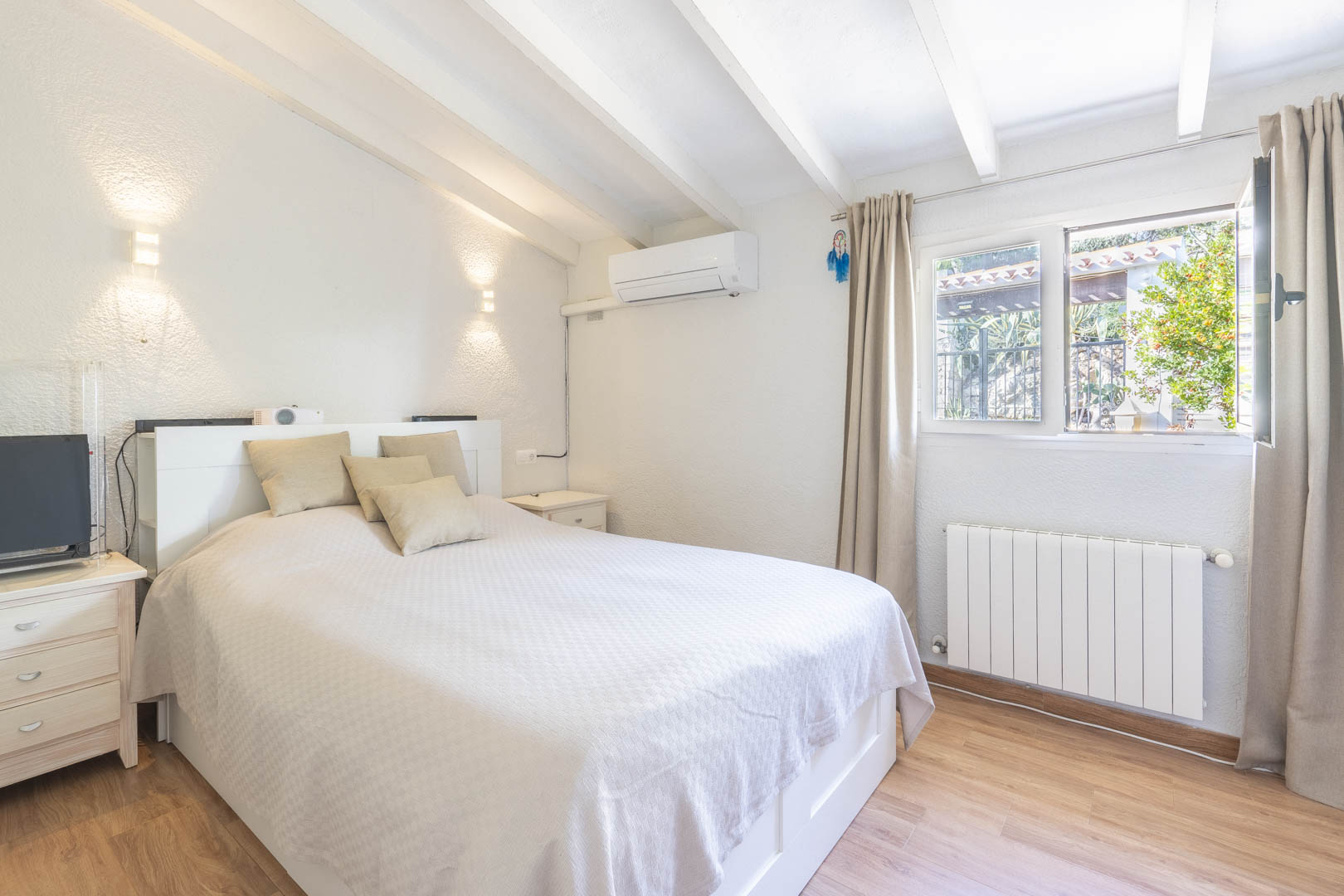 Slaapkamer met wit balkenplafond, airconditioning en radiator. De kamer is afgewerkt met een laminaatvloer en geniet van natuurlijke lichtinval.