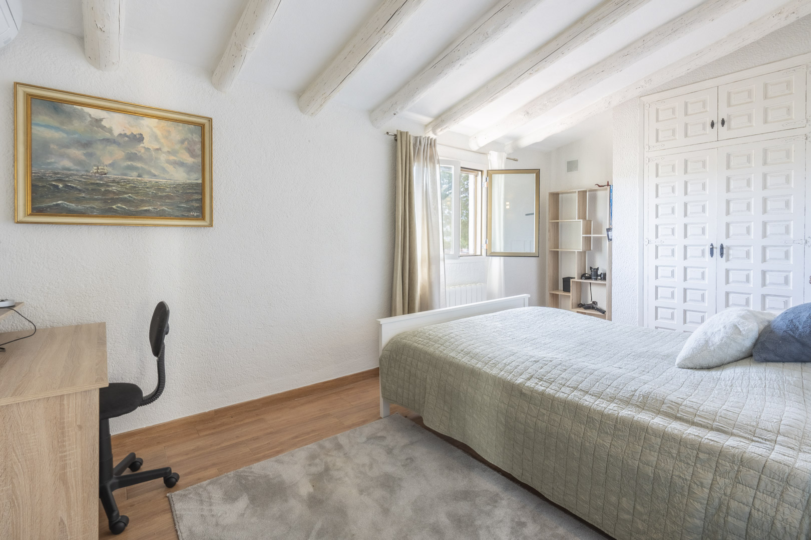 Slaapkamer met witgeschilderde houten balken, schuine plafonds, traditionele inbouwkasten en een lichte werkplek bij het raam.