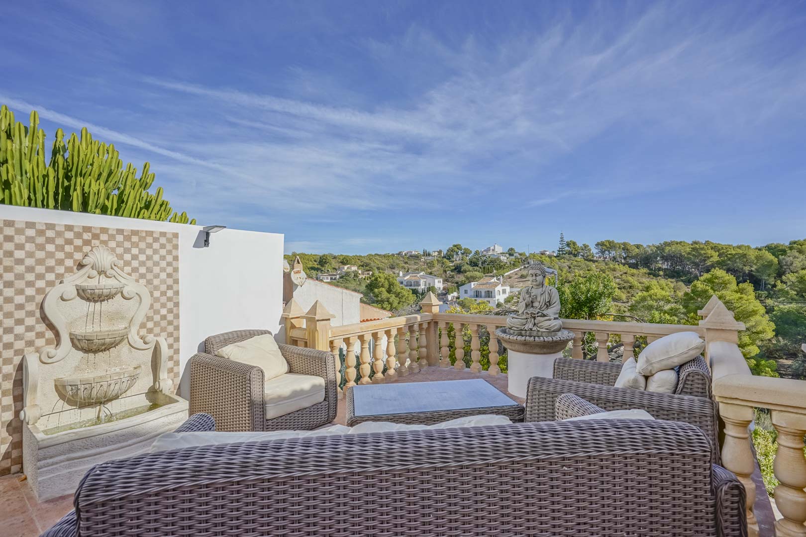 Verhoogd terras met rotan meubilair, een decoratieve wandfontein en stenen balustrades met vrij uitzicht over de groene omgeving van Jávea.