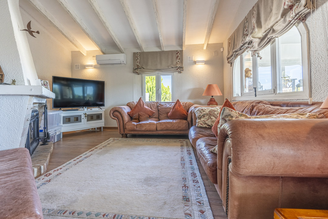 Woonkamer met wit geschilderde houten balken, lederen banken, een bakstenen open haard en wandgemonteerde airconditioning.