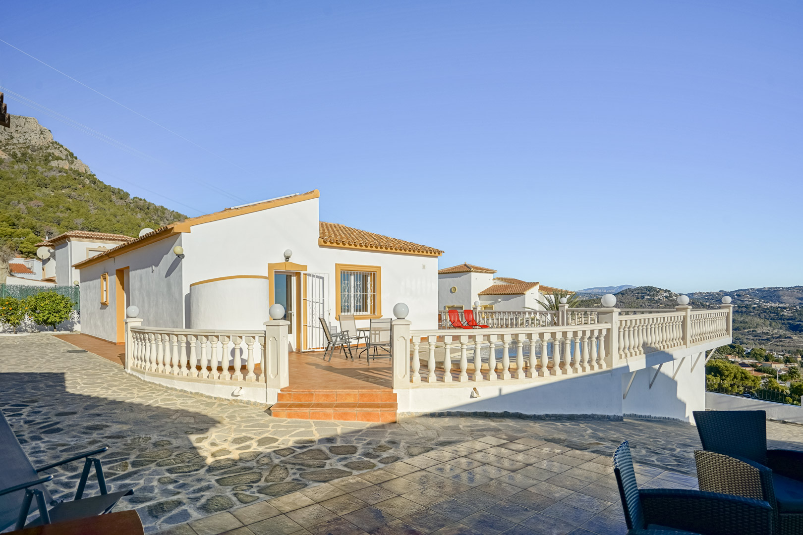 Buitenaanzicht van de villa met een ruim terracotta terras, klassieke balustrade en panoramisch uitzicht op de kustlijn en de Sierra de Oltà.