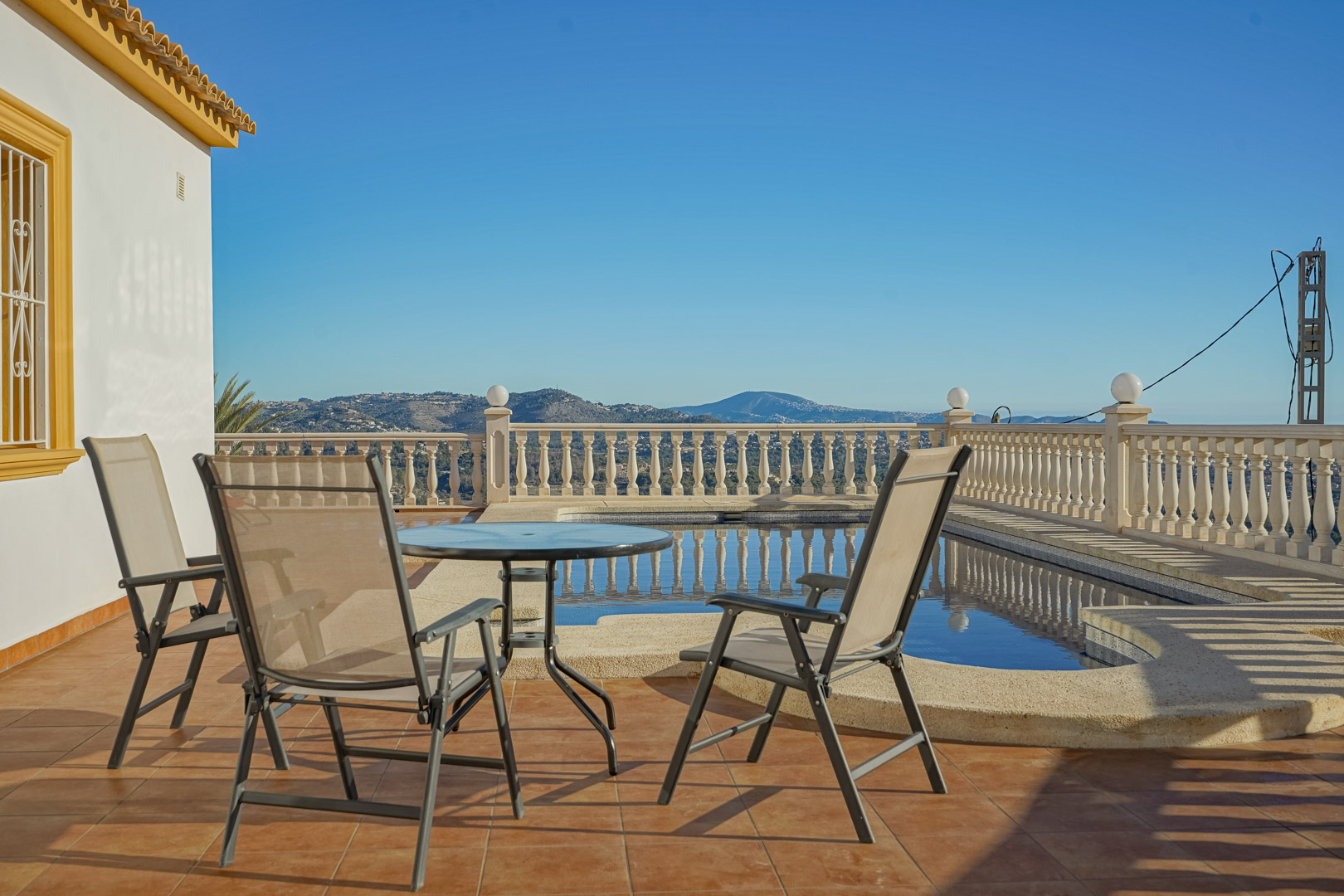 Buitenterras met terracotta tegels, een zithoek en een privézwembad omgeven door een klassieke balustrade met panoramisch uitzicht op de bergen.