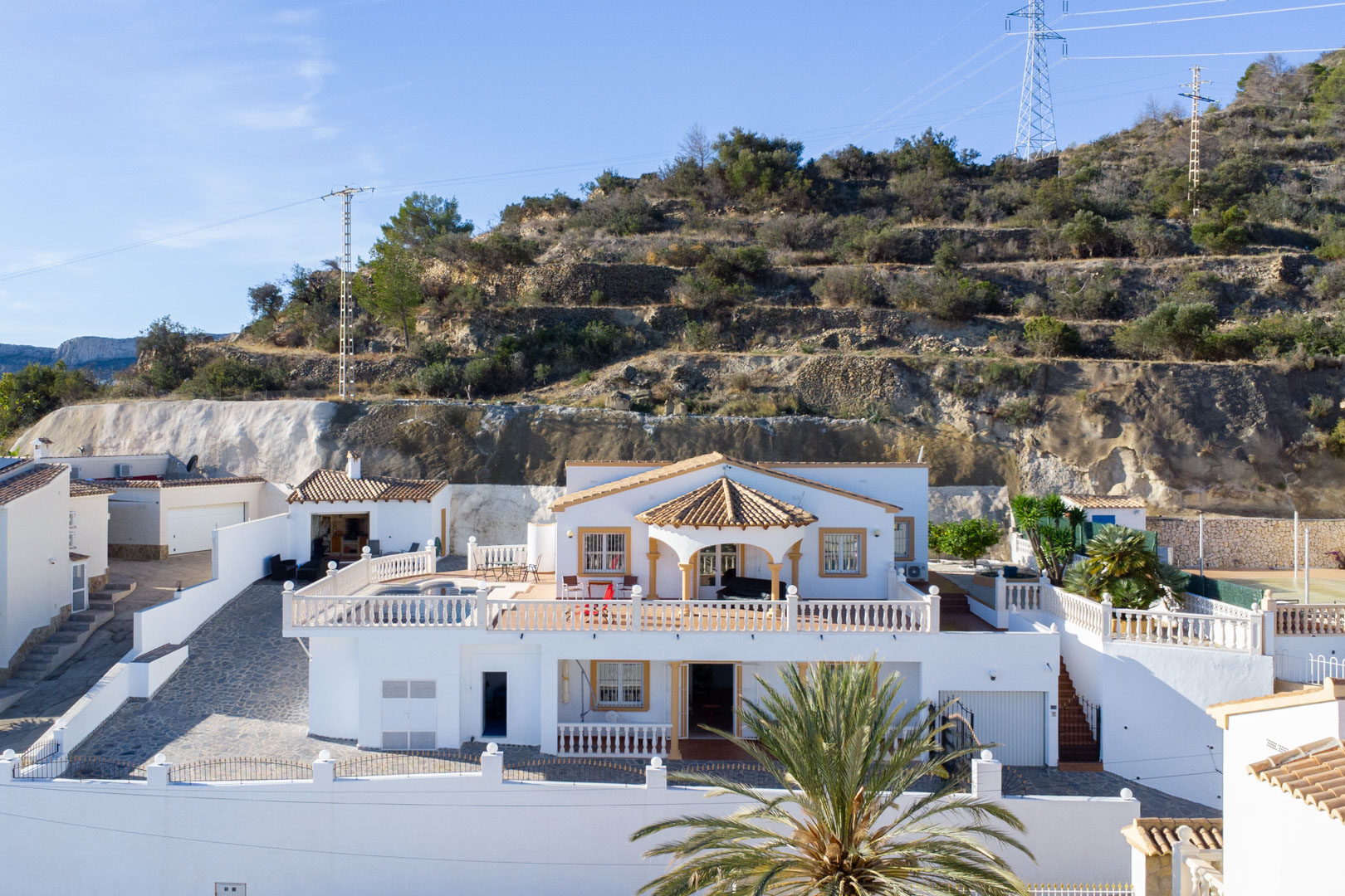 Exterieur van de witte villa met twee verdiepingen, ruime terrassen met balustrades, privézwembad en buitenkeuken tegen de helling van de Sierra de Oltà.