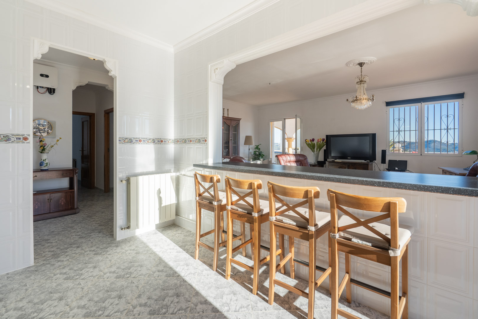 Keukenbar met houten krukken en uitzicht op de woonkamer, voorzien van wit betegelde wanden, traditionele bogen en uitzicht op de bergen door het raam.