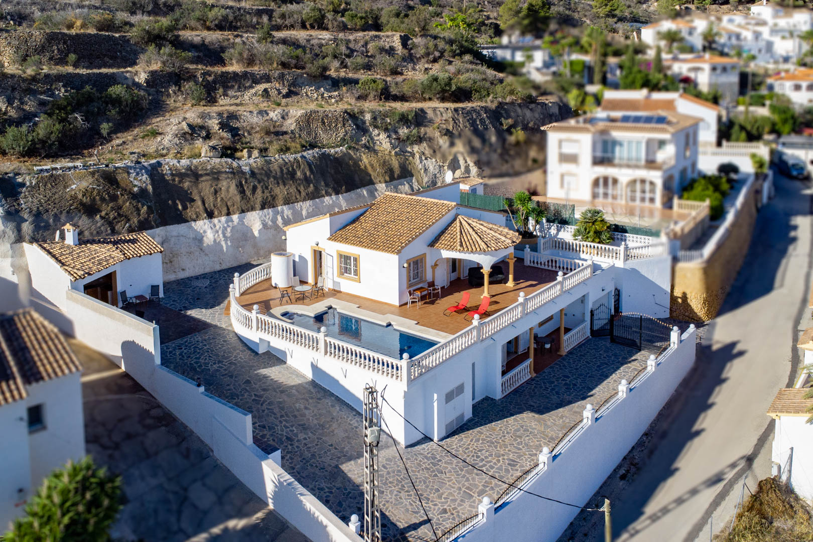 Luchtfoto van de villa met privézwembad op een verhoogd terras, witte balustrades, terracotta dakpannen en een ruime, met natuursteen geplaveide binnenplaats.