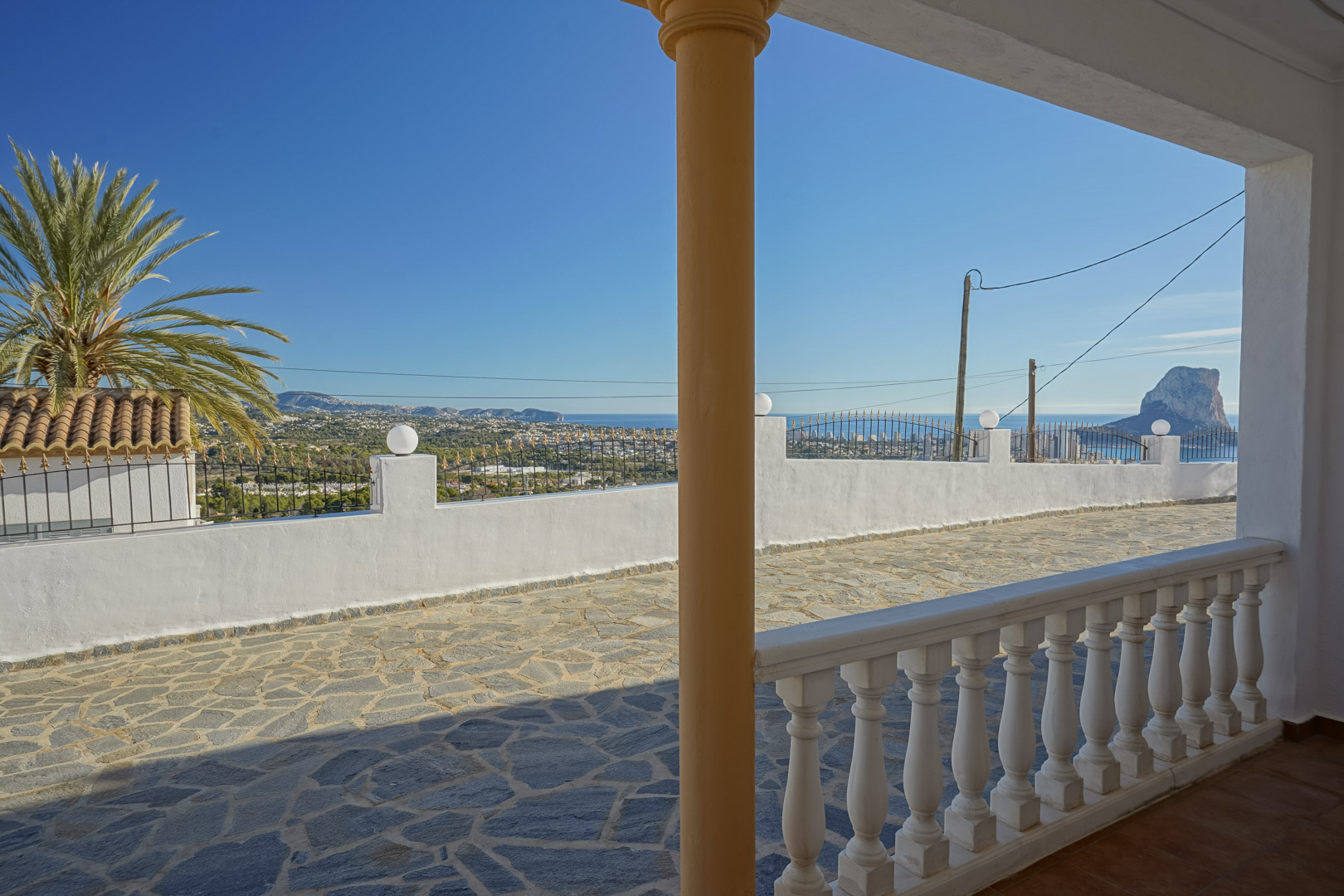 Panoramisch uitzicht vanaf de overdekte veranda met witte balustrade, uitkijkend over het natuurstenen terras en de iconische Peñón de Ifach in Calpe.