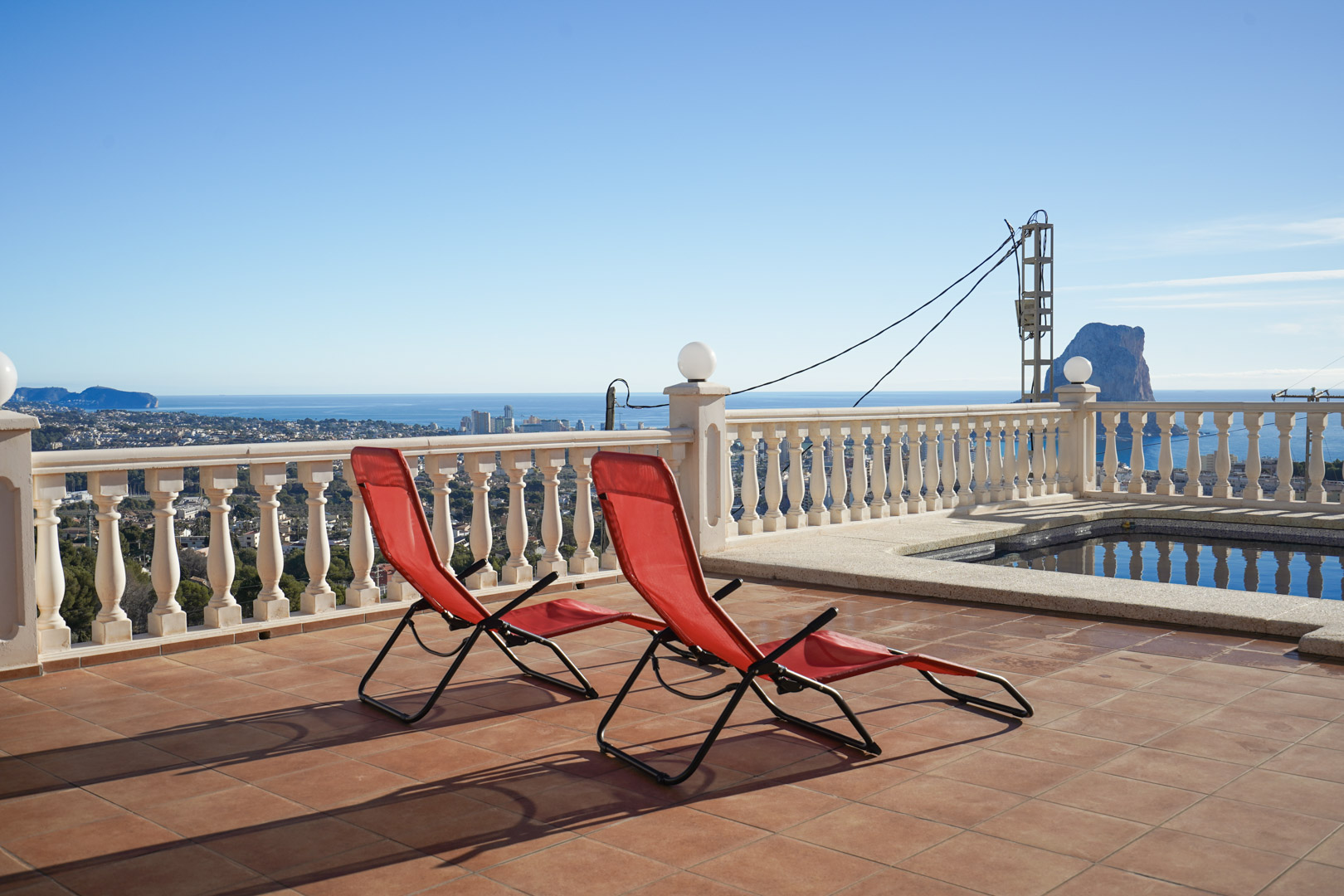 Verhoogd terras met terracotta tegels, witte balustrade en panoramisch uitzicht op de Peñón de Ifach en de Middellandse Zee bij het zwembad.