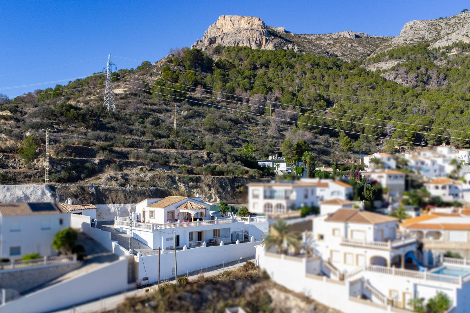 Verhoogd zicht op de witte villa aan de voet van de Sierra de Oltà, met traditionele architectuur, pannendaken en ruime terrassen.