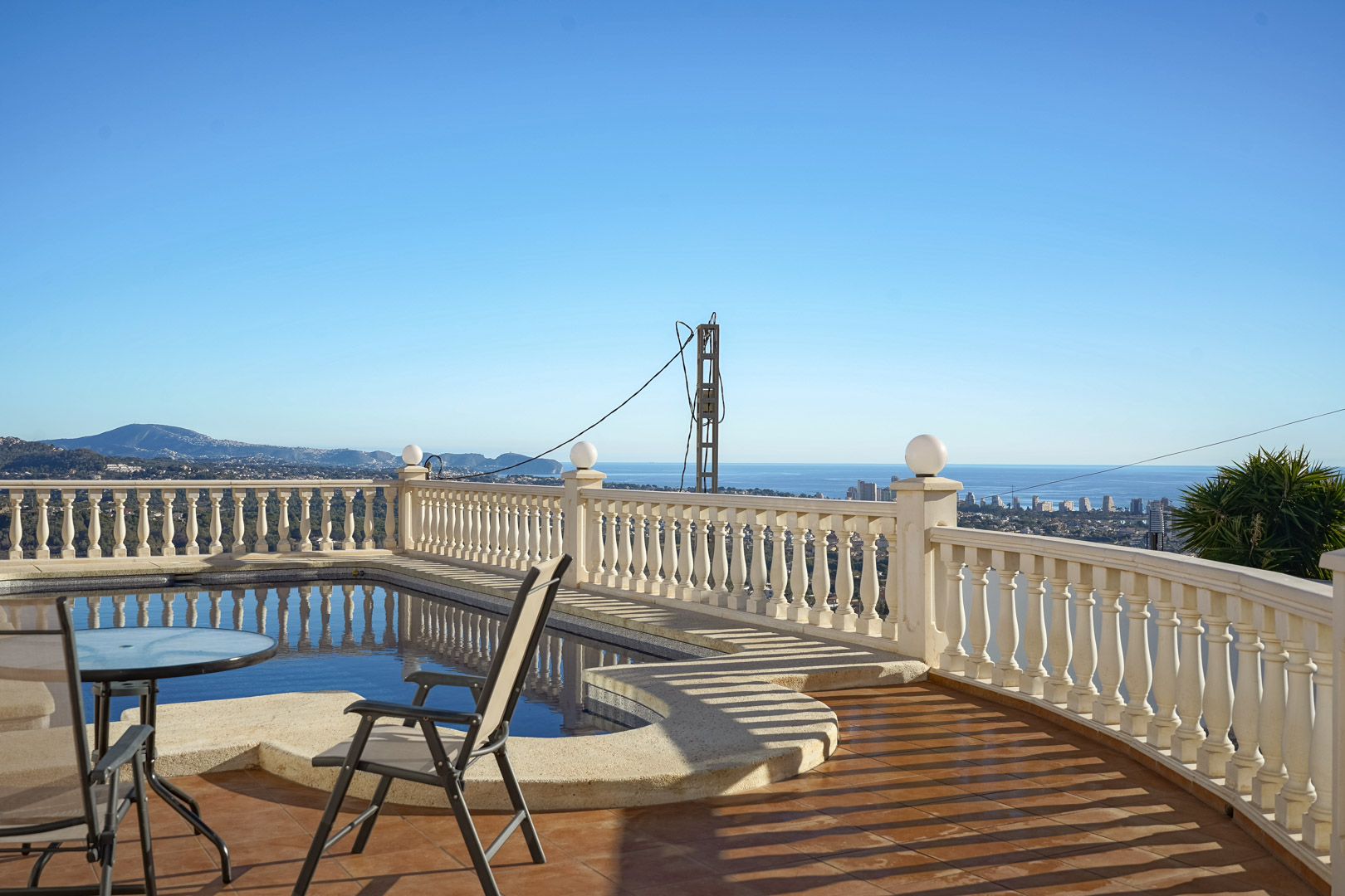 Zwembadterras met klassieke balustrade en terracotta tegels, met panoramisch uitzicht op de Middellandse Zee en de skyline van Calpe.