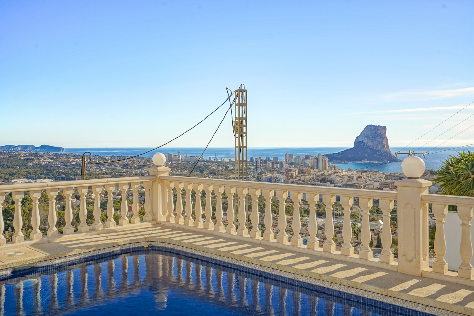 Zwembadterras met klassieke stenen balustrade en panoramisch uitzicht op de Peñón de Ifach, de skyline van Calpe en de Middellandse Zee.
