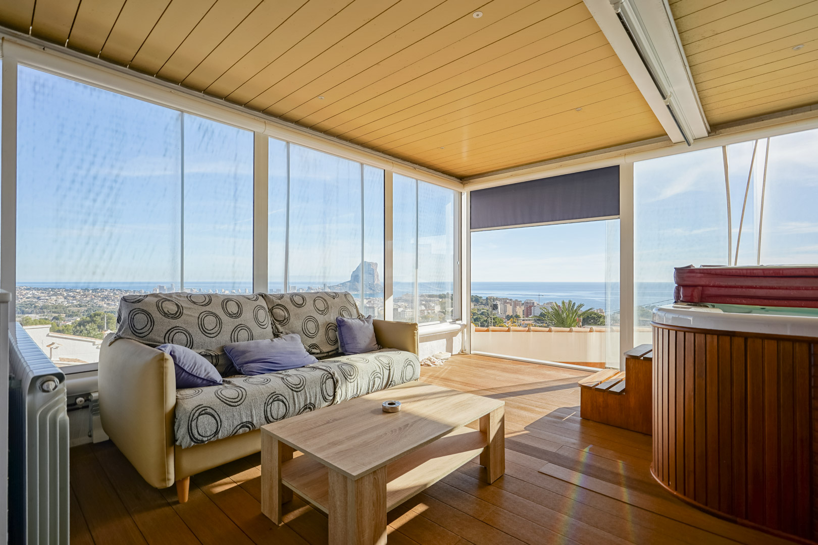 Beglaasd boventerras met jacuzzi, houten vloer en panoramisch uitzicht op de Peñón de Ifach. Voorzien van een zithoek en kamerhoge glazen wanden.