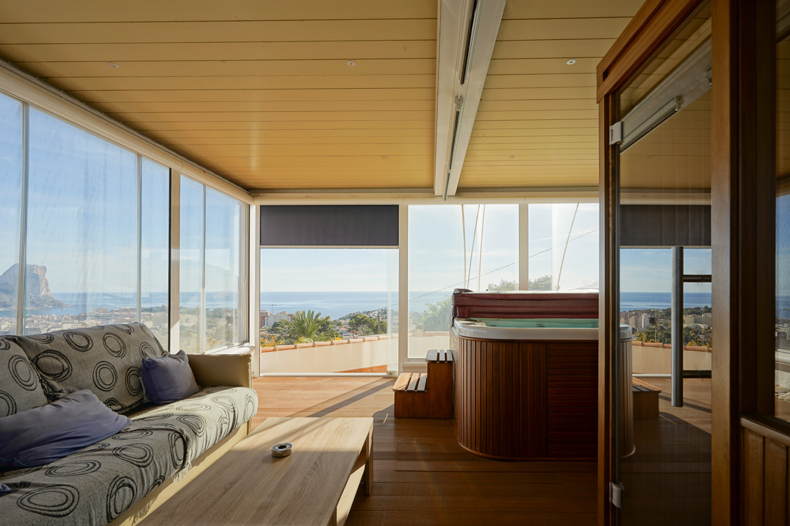 Beglaasd terras met een met hout beklede jacuzzi, zithoek en panoramisch uitzicht op de Peñón de Ifach. Voorzien van houten vloeren en een plafond met inbouwspots.