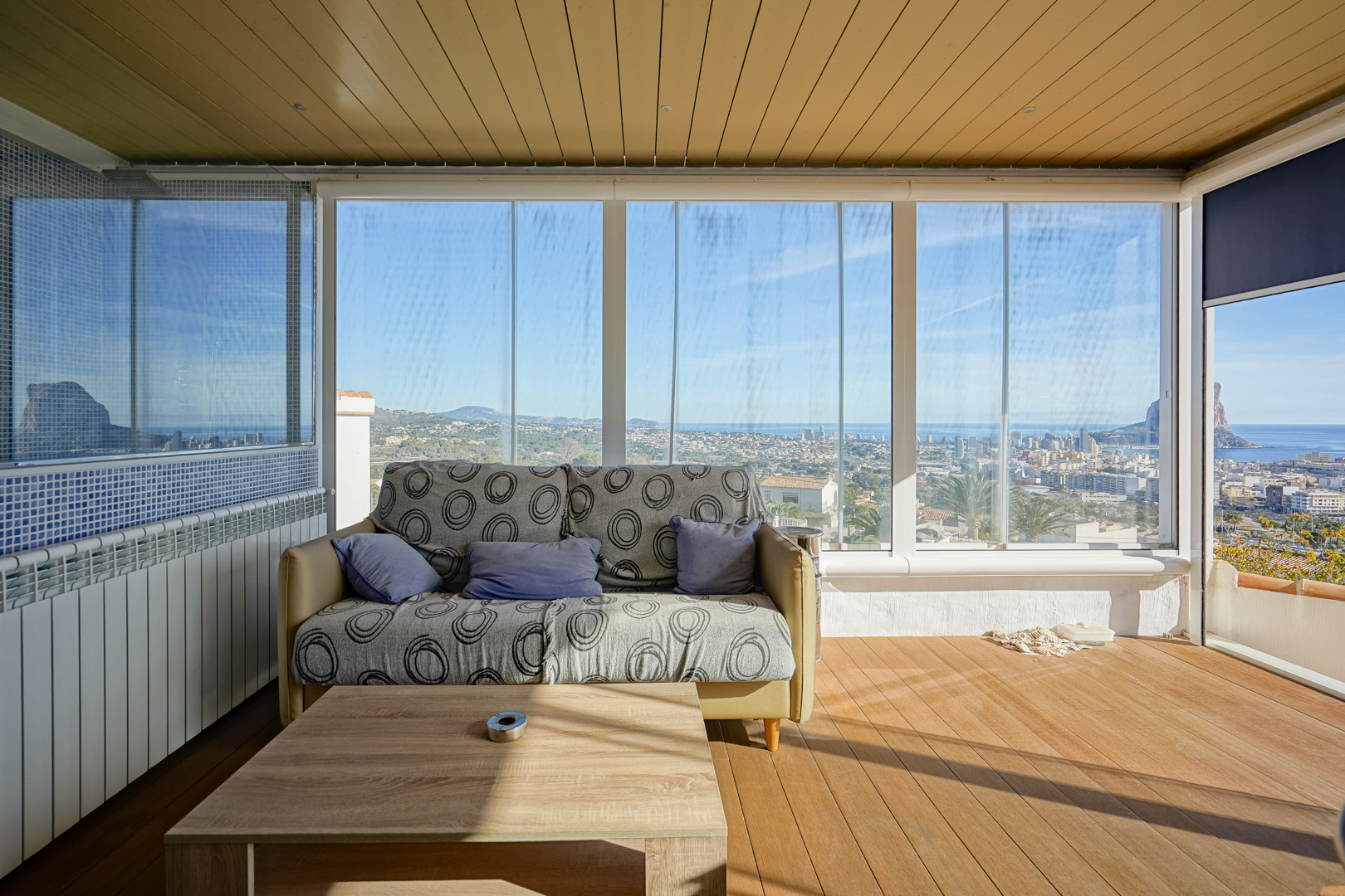 Beglaasd terras met glazen gordijnen, houten vloer en panoramisch uitzicht op de skyline van Calpe en de Peñón de Ifach. Voorzien van een houten plafond en zithoek.