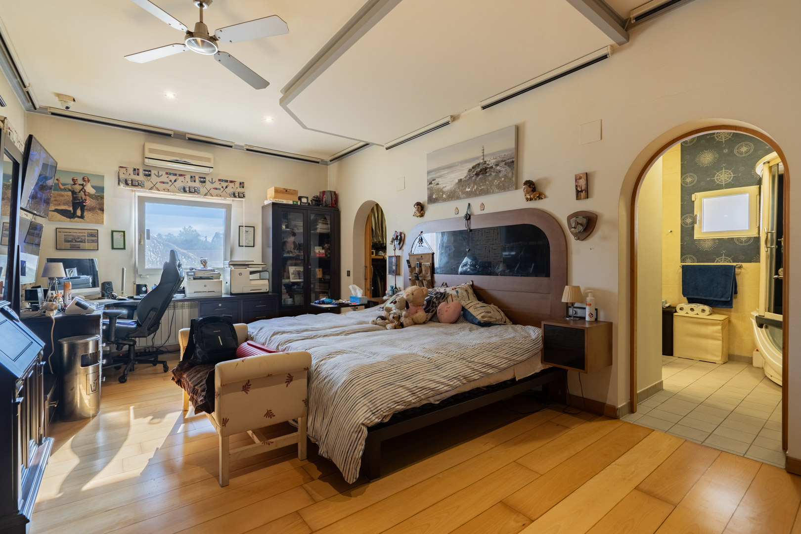 Hoofdslaapkamer met hardhouten vloeren, een geïntegreerde werkruimte en aangrenzende badkamer. Voorzien van een plafondventilator en airconditioning.