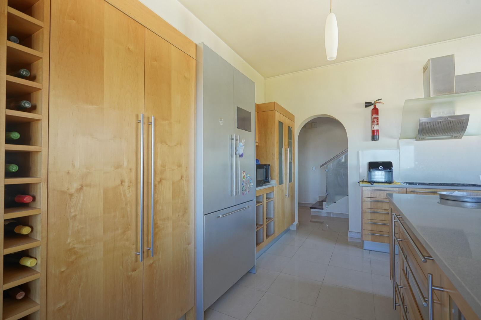 Keuken met op maat gemaakte houten kasten, een ingebouwd wijnrek en roestvrijstalen apparatuur. De boogvormige doorgang leidt naar de trap met een glazen balustrade.