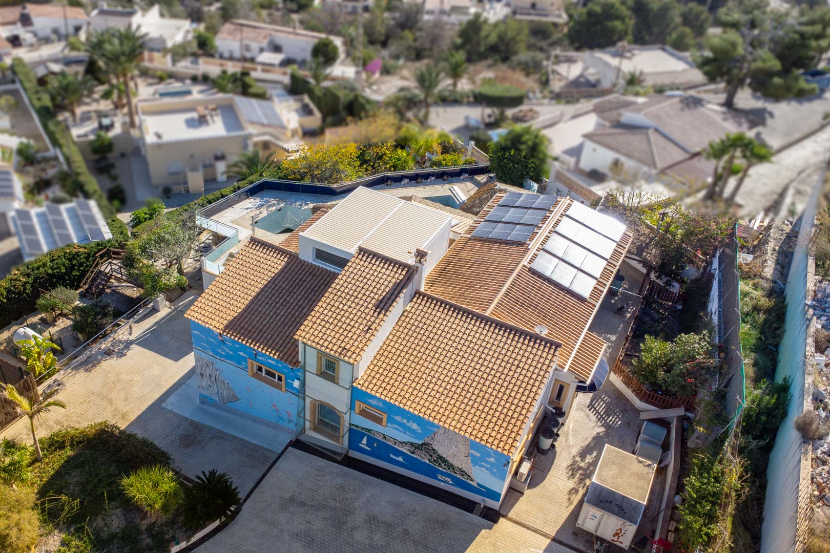 Luchtfoto van de villa met het traditionele pannendak, de zonnepanelen en een gedetailleerde muurschildering van de Peñón de Ifach op de zijgevel.