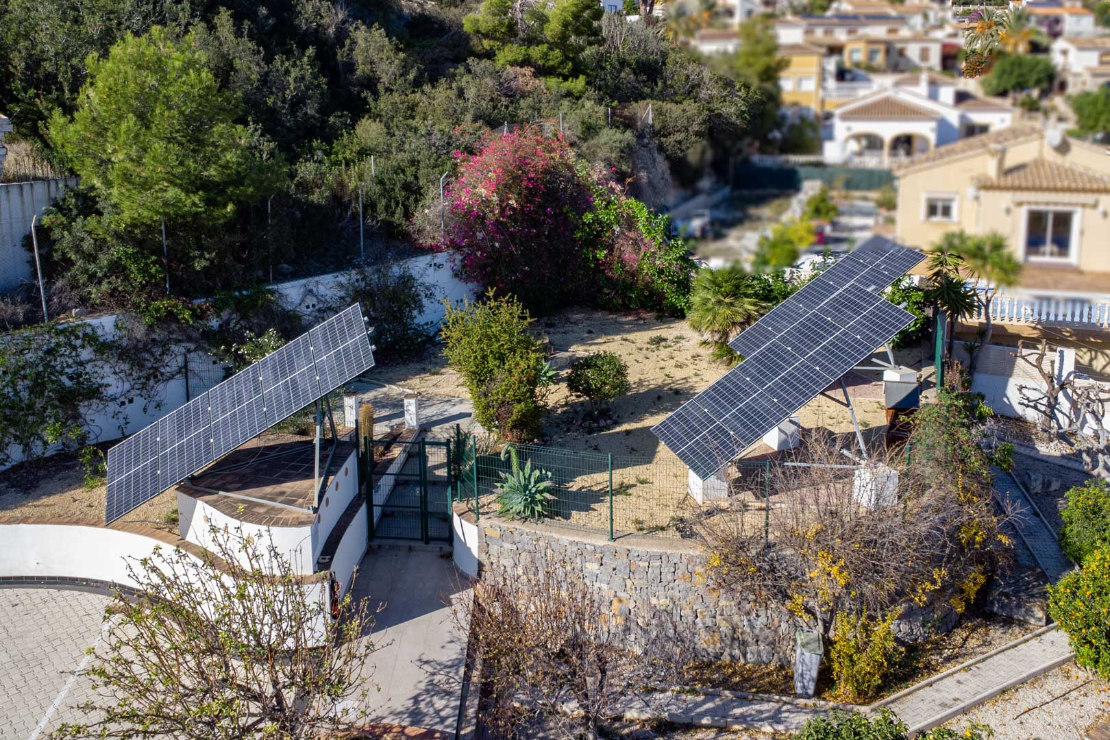 Luchtfoto van het geavanceerde fotovoltaïsche systeem met drie gemotoriseerde zonnetorens op het perceel, omgeven door mediterrane tuinen en stenen muren.