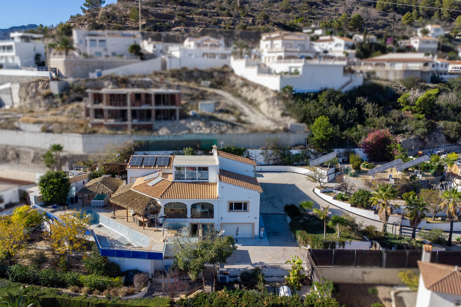Luchtfoto van het landgoed met de drie gemotoriseerde zonnetorens, de ruime geplaveide oprit en de terrassen met rieten pergola's bij het zwembadgedeelte.
