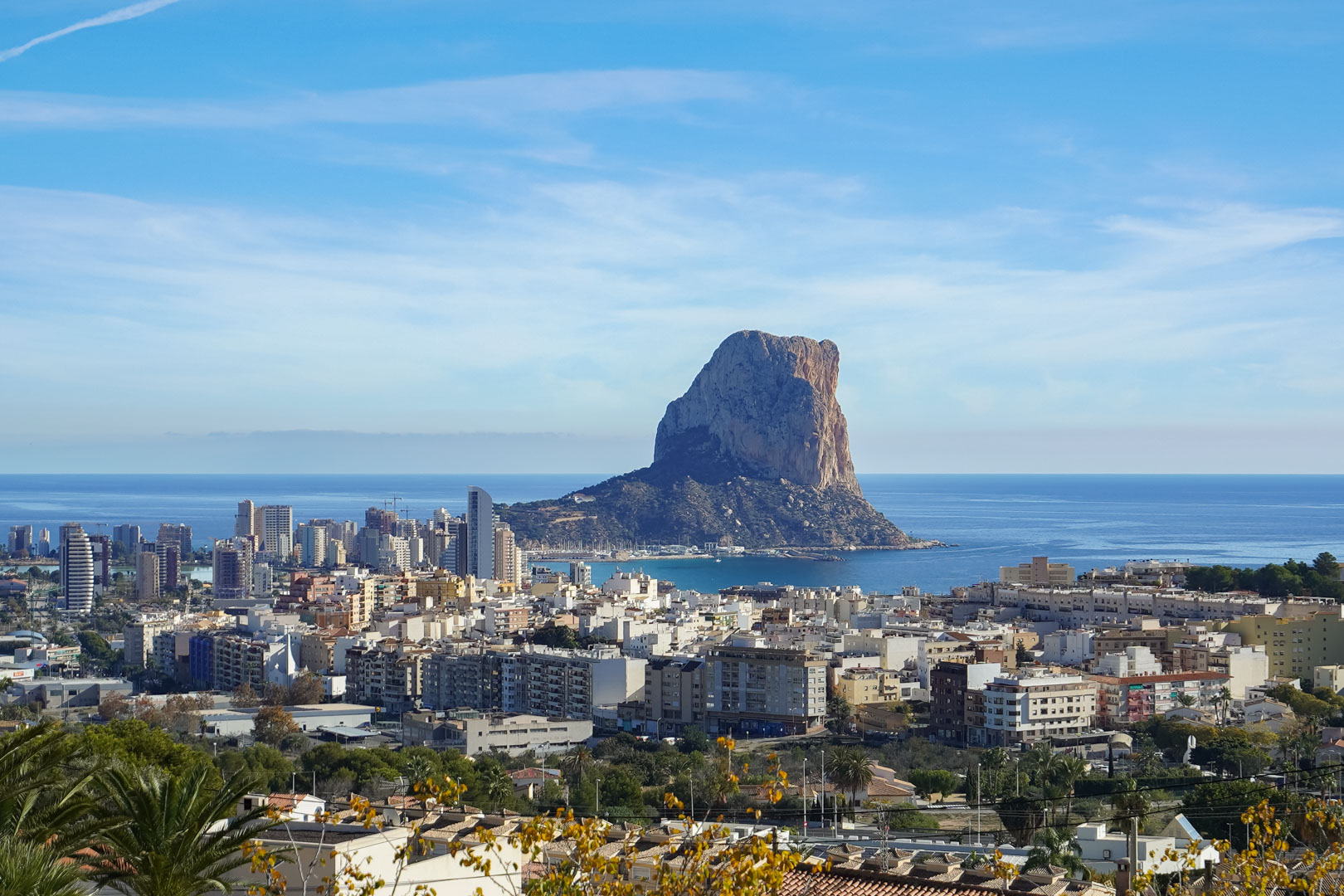 Panoramisch uitzicht op de Peñón de Ifach en de skyline van Calpe vanaf een verhoogde positie, met de Middellandse Zee en de kuststad op de voorgrond.