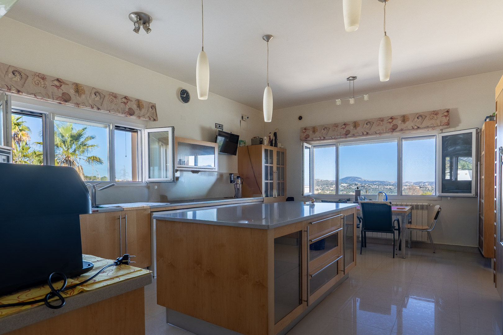 Ruime keuken met een groot kookeiland van hout en grijze werkbladen. Grote ramen bieden een panoramisch uitzicht op de zee en de omliggende bergen.