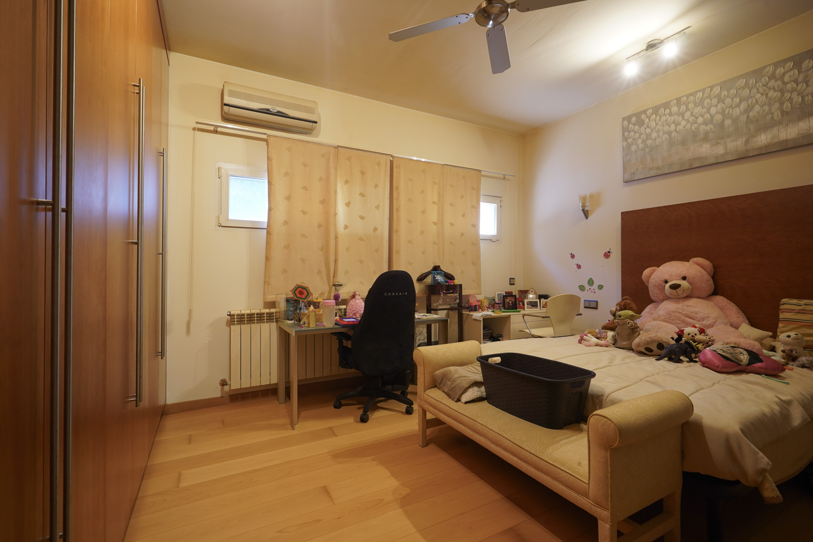 Slaapkamer met hardhouten vloeren, ruime ingebouwde houten kasten, een bureaugedeelte, airconditioning en een plafondventilator.