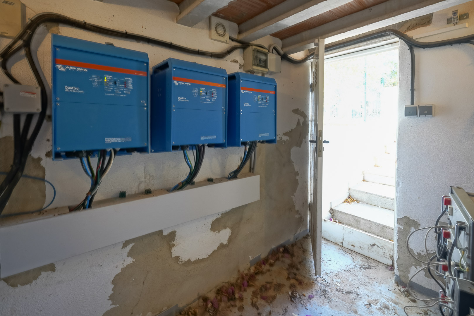 Technische ruimte met drie Victron Energy Quattro omvormers voor de zonne-energie-installatie, gelegen nabij een open buitendeur.