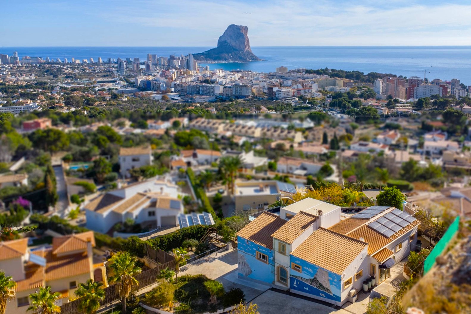 Verhoogd aanzicht van de villa met zonnepanelen en muurschildering, uitkijkend over de skyline van Calpe en de iconische Peñón de Ifach.